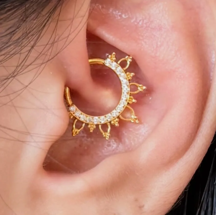 Close-up of a daith piercing with a crystal-paved gold ring finished with beaded lotus points