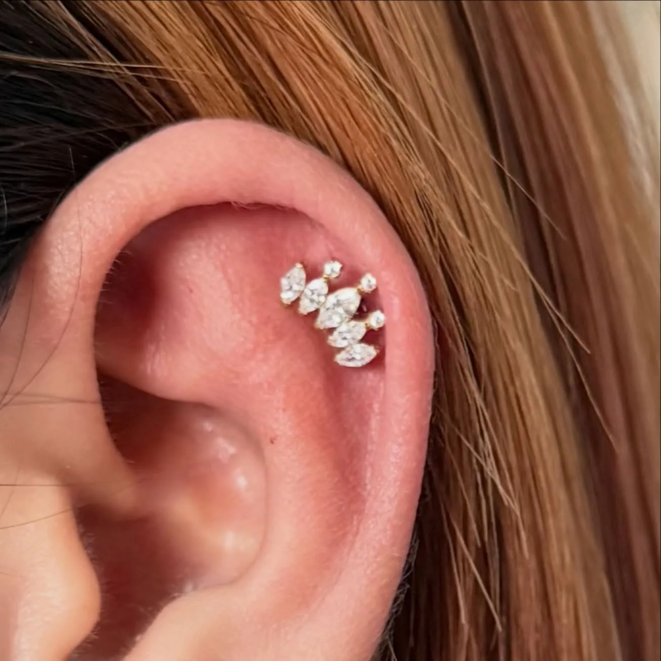 Upper cartilage piercing with a gold crown-style cluster of marquise crystals