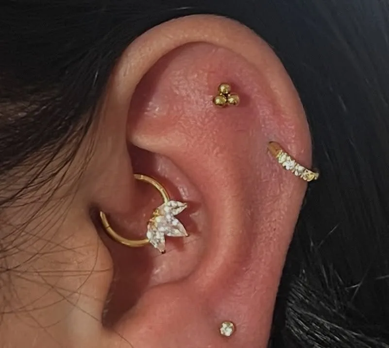 Curated ear with a gold crystal-leaf daith ring, trinity bead stud, and pave hoop on the upper cartilage