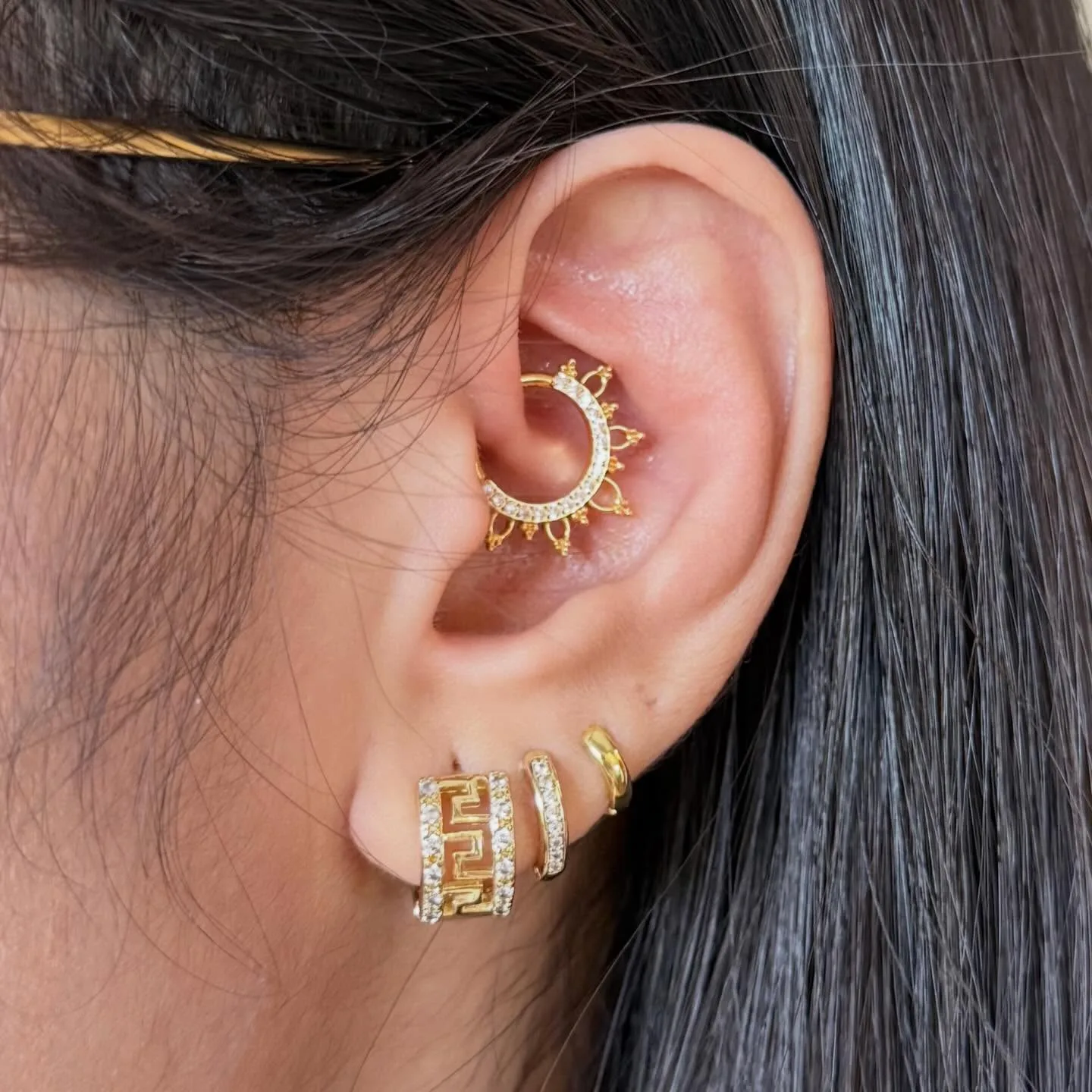 Daith piercing with an ornamental gold clicker ring, styled with three gold huggie hoops on the lobe